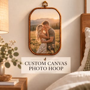 May include: A rectangular canvas photo print featuring a couple embracing in a field at sunset, enclosed in a dark brown wooden hoop frame with a small metal hanging loop at the top. The text CUSTOM CANVAS PHOTO HOOP is printed below.