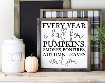 May include: A white ceramic coffee jar with a lid, a small orange pumpkin, and a framed sign with the text "EVERY YEAR i fall for PUMPKINS, SMORES, BONFIRES, AUTUMN LEAVES ...and you...." on a wooden shelf.
