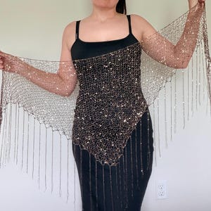 May include: A brown mesh shawl with sparkling embellishments and long fringe. The shawl is draped over a black dress. The mesh is a dark brown color, and the embellishments are silver.