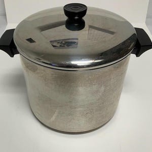 May include: A stainless steel cooking pot with a lid and black handles. The pot has a shiny, reflective surface and a black knob on the lid. The pot is designed for cooking and food preparation.