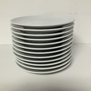 May include: A stack of white, round plates. The plates are stacked neatly on top of each other, with the edges of each plate visible. The plates are made of a smooth, glossy material and are likely ceramic or porcelain. The plates are clean and appear unused.