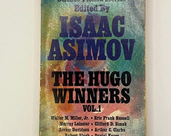 May include: A vintage paperback book titled "The Hugo Winners Vol. 1" edited by Isaac Asimov. The cover features a colorful, abstract background with bold text in blue and orange. Authors' names are listed below the title.