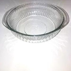 May include: Clear glass baking dish with a round shape and ribbed sides. The dish has two handles and a flat bottom. The glass is transparent, allowing visibility of the contents. Ideal for baking and serving.