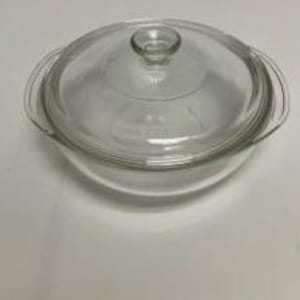 May include: A clear glass casserole dish with a matching lid. The round dish features two integrated side handles and a circular lid with a central knob handle. The glass is transparent, smooth, and has a simple, functional design for cooking.