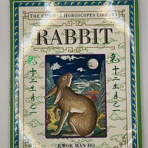 May include: A book from "The Chinese Horoscopes Library" featuring a brown rabbit illustration under a night sky with a full moon. The cover has the title "RABBIT" and the author's name, "KWOK MAN-HO". The book has a green border.