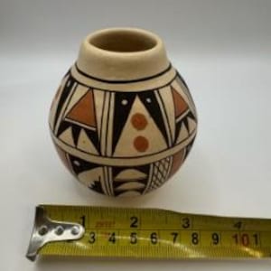 May include: A small, round ceramic vase with a cream-colored base and a geometric design in black, brown, and cream. The vase is approximately 4 inches tall and 4 inches wide. The design includes triangles, lines, and dots.