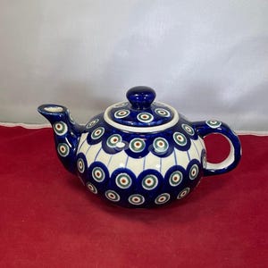 May include: A blue and white ceramic teapot with a peacock design. The teapot has a round body and a spout on the side. The handle is on the opposite side of the spout.