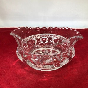 May include: A clear glass bowl with a scalloped edge and a raised pattern of small circles. The bowl is sitting on a red velvet surface.