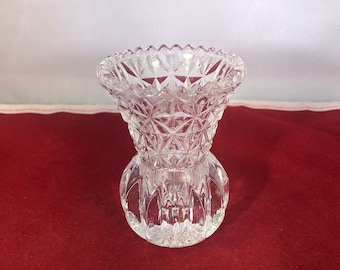 May include: A clear glass bud vase with a diamond pattern. The vase is small and has a round base.