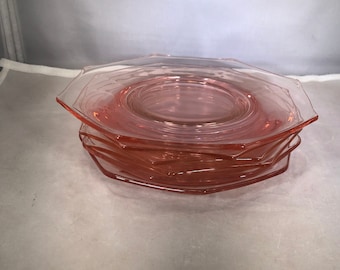 May include: A stack of six pink glass dessert plates with a scalloped edge.