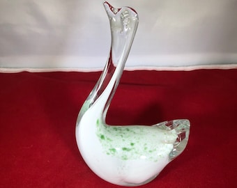 May include: A white glass swan figurine with green flecks throughout the body. The swan has a long neck and a small head.