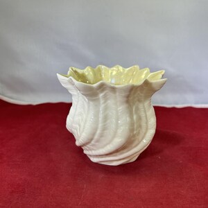 May include: A white ceramic vase with a yellow glaze and a shell-like design.