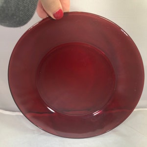May include: A deep red glass dinner plate. The plate is round and has a slightly raised rim.
