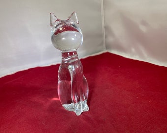 May include: A clear glass cat figurine. The cat is sitting with its tail curled around its legs. The figurine is made of clear glass and has a smooth, polished finish.