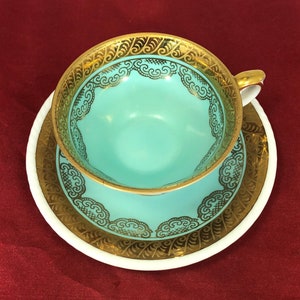 May include: A turquoise teacup and saucer with a gold rim and intricate gold floral design.