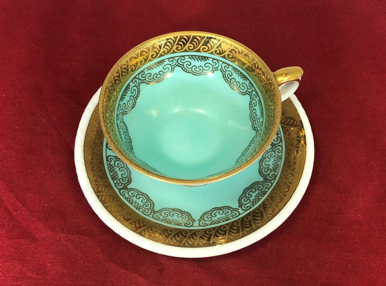 May include: A turquoise teacup and saucer with a gold rim and intricate gold floral design.