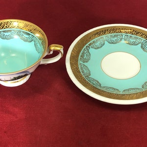 May include: A turquoise teacup and saucer set with gold trim and a floral design. The cup has a small handle and a base. The saucer has a wide rim.