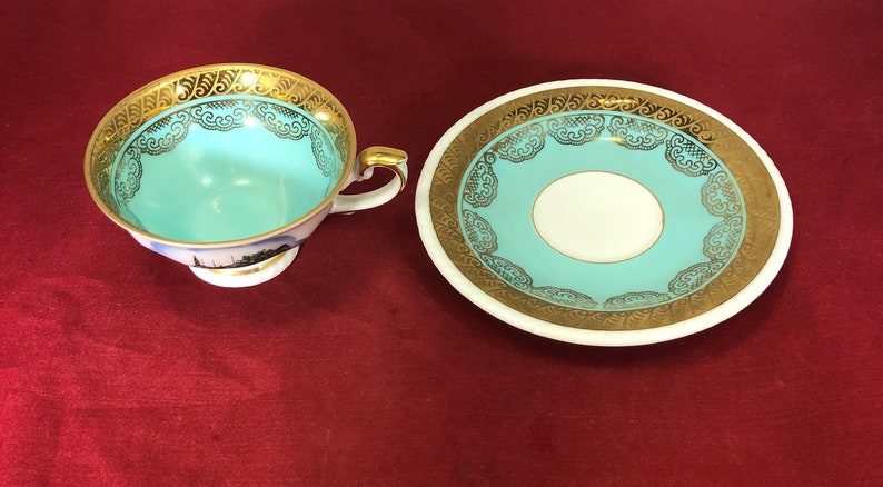 May include: A turquoise teacup and saucer set with gold trim and a floral design. The cup has a small handle and a base. The saucer has a wide rim.