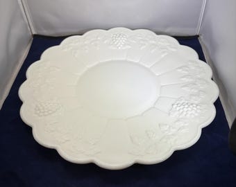 May include: A white, scalloped-edge serving platter with embossed grape and vine designs. The center of the platter is smooth, while the rim features a repeating pattern of grapes and leaves. This decorative dish is ideal for serving appetizers or desserts.