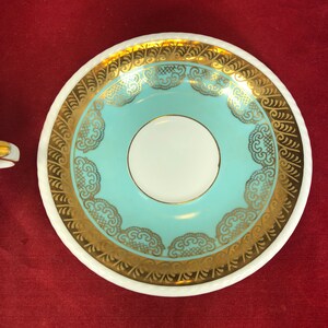 May include: A white saucer with a light blue center and gold trim. The trim features a delicate lace pattern.