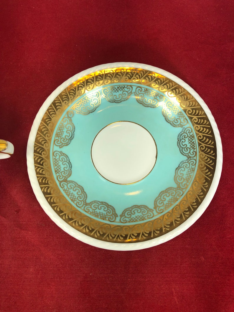 May include: A white saucer with a light blue center and gold trim. The trim features a delicate lace pattern.