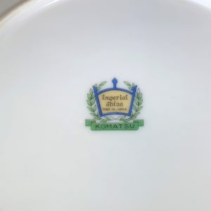 May include: A white ceramic plate with a green and blue logo that reads "Imperial China Made in Japan" and "Komatsu" in a banner.