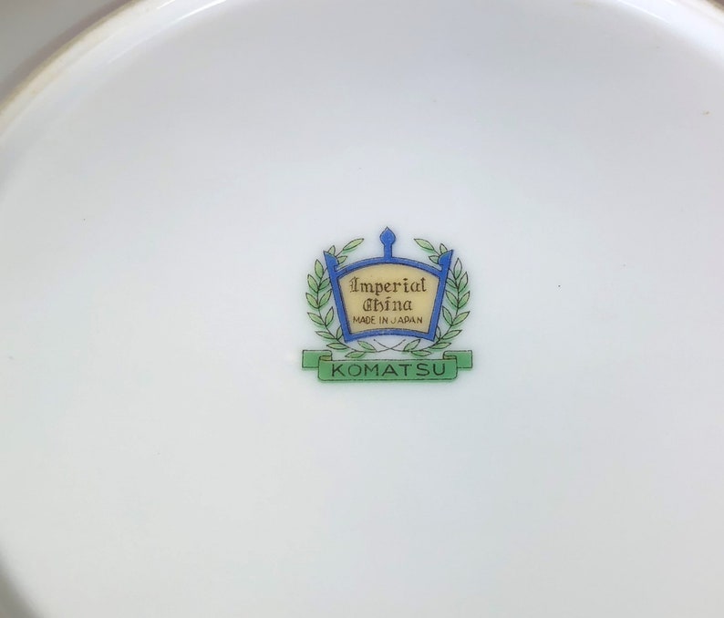 May include: A white ceramic plate with a green and blue logo that reads "Imperial China Made in Japan" and "Komatsu" in a banner.