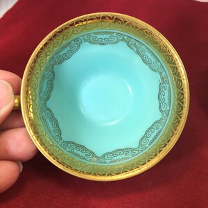 May include: A turquoise teacup with a gold rim and intricate gold design. The design features a repeating pattern of stylized clouds.