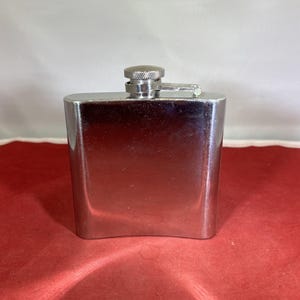 May include: A silver metal hip flask with a screw-on cap.
