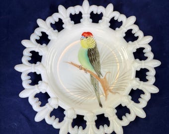 May include: White decorative plate with a scalloped edge. The plate features a hand-painted bird perched on a branch. The bird has a red head, yellow chest, and green and gray body. The plate is on a dark blue background.