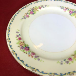 May include: A white ceramic plate with a floral design. The plate has a blue and gold trim and features pink, yellow, and purple flowers.
