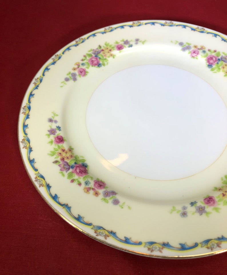 May include: A white ceramic plate with a floral design. The plate has a blue and gold trim and features pink, yellow, and purple flowers.