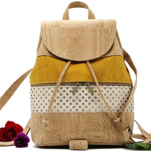 May include: A small cork backpack with a yellow, white, and brown color scheme. The backpack has a drawstring closure and two zippered pockets. The backpack is made of cork and has a cork strap.