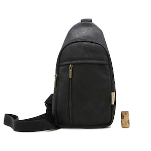 May include: Black sling bag with a zippered front pocket and adjustable strap. The bag has a gold zipper and a small cork next to it. The bag is made of a textured material.