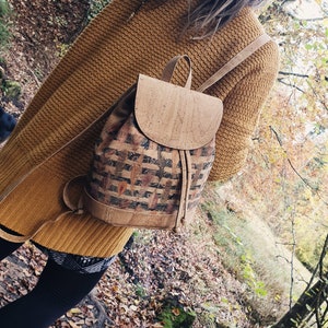 May include: A cork backpack with a brown and black patterned design. The backpack has a drawstring closure and a flap with a buckle.