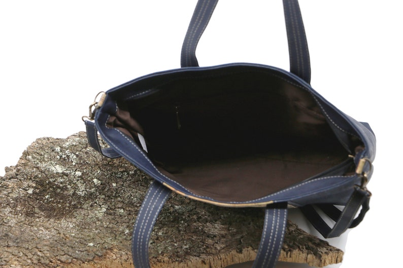 May include: A navy blue tote bag with a brown lining and a zipper closure. The bag has two top handles and a detachable shoulder strap.