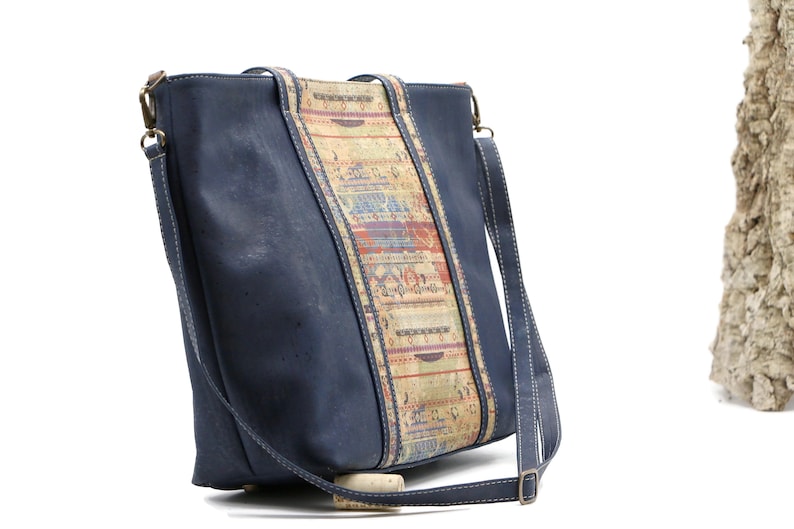May include: A blue cork leather tote bag with a patterned cork strap. The bag has a long shoulder strap and a top zipper closure.