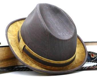 May include: A brown fedora hat with a yellow band and a brown leather strap. The hat is made of cork and has a slightly distressed look.