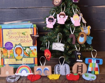 Può includere: Un piccolo albero di Natale decorato con ornamenti in feltro, tra cui angeli, un leone e una stella. Una copia di "The Jesus Storybook Bible" è nelle vicinanze. Gli ornamenti sono di varie forme e colori.