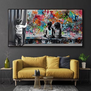Op de afbeelding: Een rechthoekige wandkunstprint met een zwart-witillustratie van een kind dat een gordijn opzij trekt om twee kinderen te onthullen die voor een levendige, veelkleurige muur vol graffiti met abstracte tags en symbolen zitten.