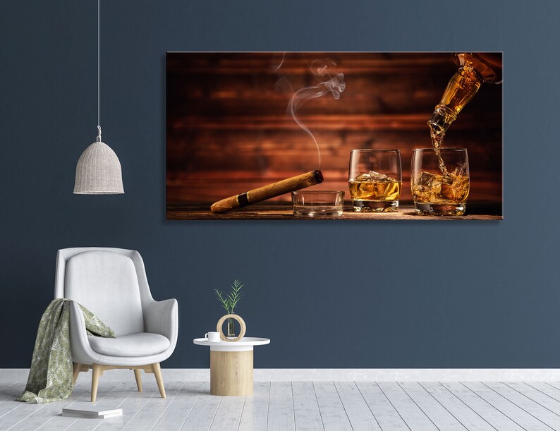 May include: A wooden background with two glasses of amber liquid, one being poured from a bottle. A cigar rests on the surface in front of the glasses.