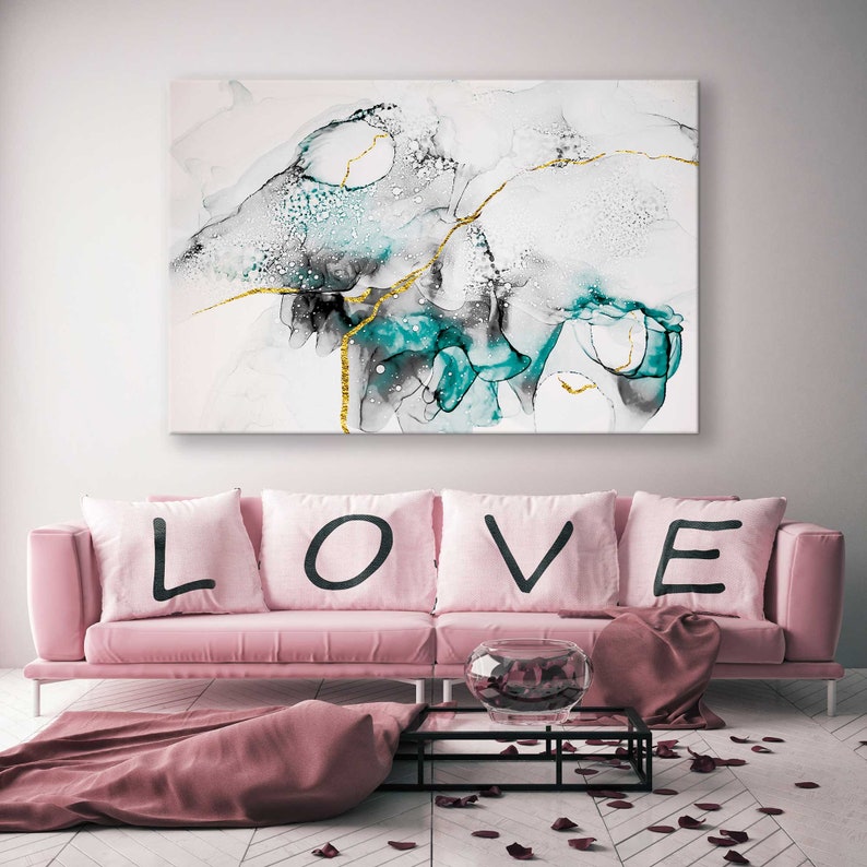 May include: A pink sofa with four cushions spelling out "LOVE" in black lettering. The sofa is in front of a white wall with a large abstract painting featuring teal, black, and gold accents.