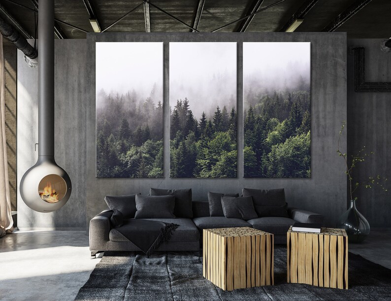Puede incluir: Una impresi&oacute;n en lienzo de tres paneles que representa una escena de bosque brumoso. La impresi&oacute;n presenta un bosque verde exuberante con &aacute;rboles altos y una niebla suave y et&eacute;rea. La impresi&oacute;n est&aacute; colgada en una pared gris sobre un sof&aacute; gris y dos mesas de caf&eacute; de madera.