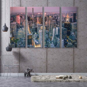 Op de afbeelding: Een vierdelige canvas print met een nachtelijke stadsgezicht. De afbeelding toont verlichte wolkenkrabbers en gebouwen, waardoor een levendige stedelijke sc&egrave;ne ontstaat. Het kleurenpalet omvat tinten blauw, oranje en paars, wat een dramatische en moderne esthetiek cre&euml;ert.