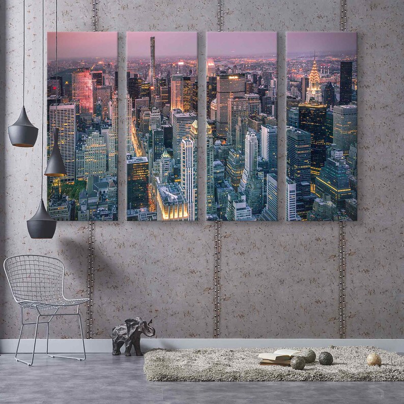 Op de afbeelding: Een vierdelige canvas print met een nachtelijke stadsgezicht. De afbeelding toont verlichte wolkenkrabbers en gebouwen, waardoor een levendige stedelijke sc&egrave;ne ontstaat. Het kleurenpalet omvat tinten blauw, oranje en paars, wat een dramatische en moderne esthetiek cre&euml;ert.