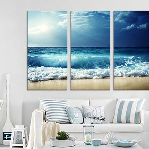 K&ouml;nnte beinhalten: Ein dreiteiliger Leinwanddruck mit einer Meereslandschaft, die blaue Wellen zeigt, die an einem Sandstrand brechen. Der Himmel ist eine Mischung aus Blau und Wei&szlig; mit Wolken.