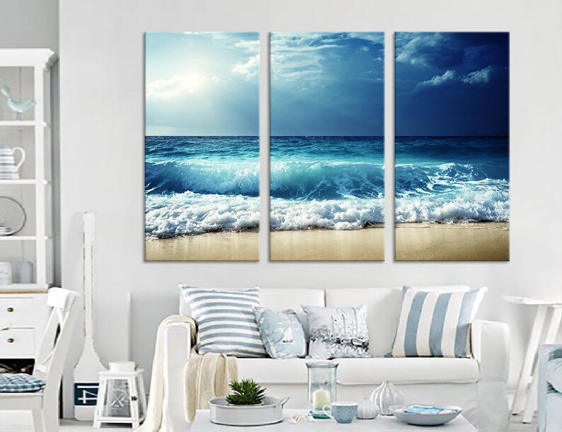 K&ouml;nnte beinhalten: Ein dreiteiliger Leinwanddruck mit einer Meereslandschaft, die blaue Wellen zeigt, die an einem Sandstrand brechen. Der Himmel ist eine Mischung aus Blau und Wei&szlig; mit Wolken.
