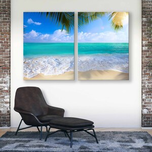 May include: Two canvas prints depicting a tropical beach scene with turquoise water, white sand, and palm trees. The prints are hung on a white wall above a brown leather armchair and footstool.