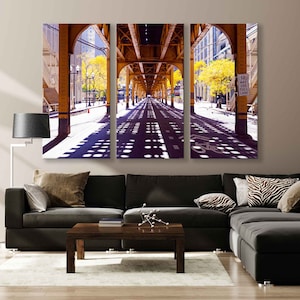 May include: A three-panel canvas print of a city street under a yellow bridge. The street is lined with trees and the sun is shining through the trees, casting shadows on the street. The street is empty except for a few cars and a bicycle lane.