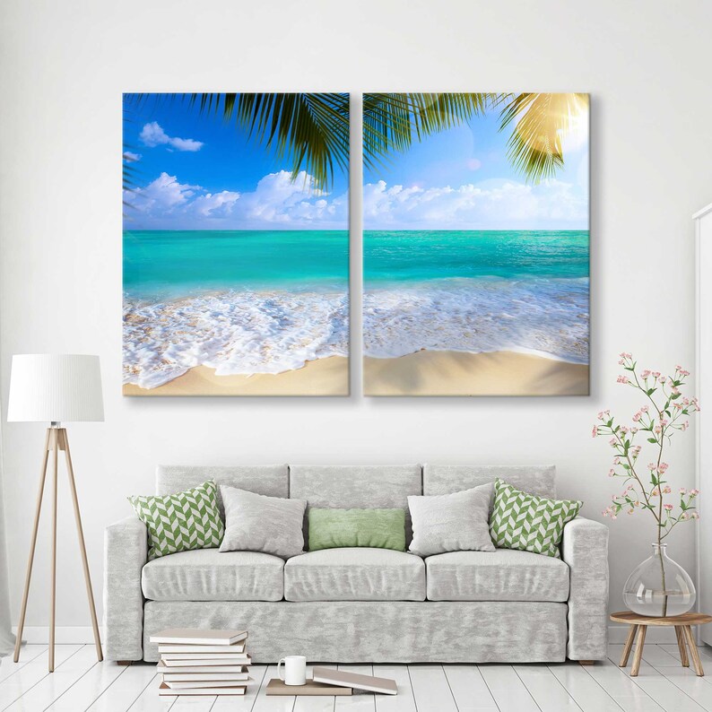 May include: A split canvas print featuring a tropical beach scene with turquoise water, white sand, and palm tree leaves. The image is divided into two panels, each showing a different perspective of the beach.